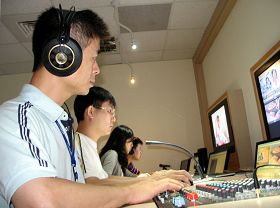 阿亮（前一）在新唐人亚太台负责成音部份。他正为晚间新闻播出的音控工作。