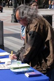 '路人驻足观看展板、接过法轮功学员派发的真相资料阅读、签名声援制止迫害'