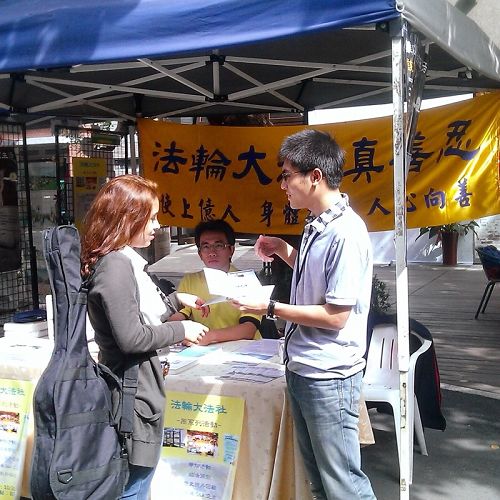 图1. 师大学生卓廷威（右一）从小过敏体质，健康不佳，悲观消极，幸于高二开始修炼法轮功，否极泰来，身心和人生观都有意想不到的改善。图为二零一四年十月师范大学校内举办法轮大法周，卓廷威向外籍交换生介绍法轮大法。